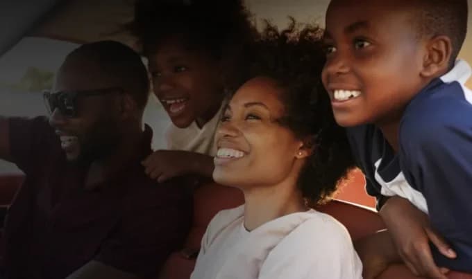 A family with husband, wife and two children similing and looking forward in a car